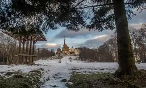 Zimowe szlaki w Górach Świętokrzyskich prowadzą do Świętej Katarzyny. Na pierwszym planie drewniana wiata z krzyżem, w oddali klasztor.