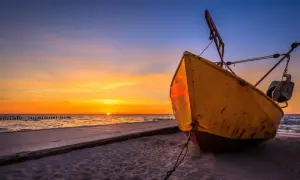 Żółta łódź na plaży w Niechorzu podczas zachodu słońca. Słońce odbija się w morzu, a niebo mieni się pomarańczem i błękitem.